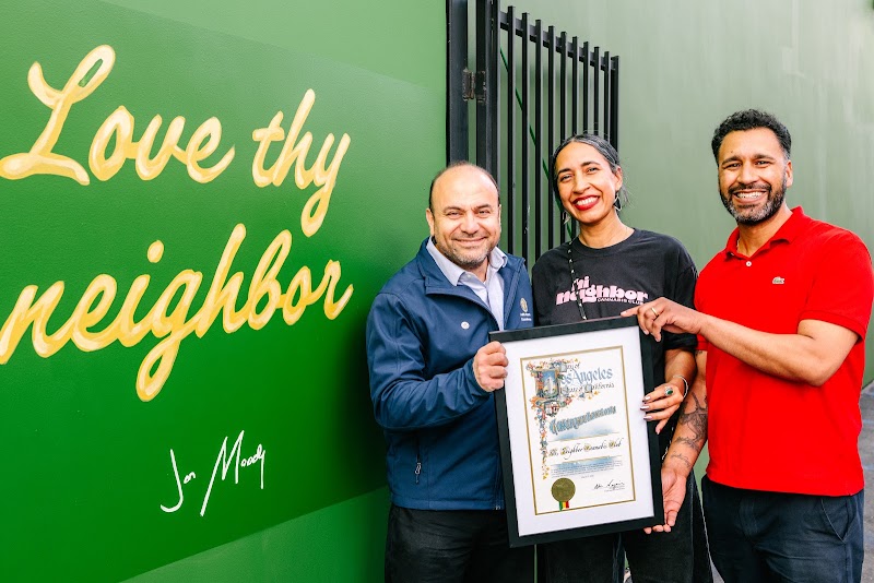 Neighbors holding a framed certificate in front of the mural